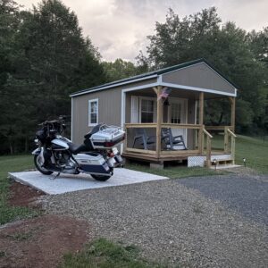 Motorcycle parked in front of a small cabin in a wooded area.